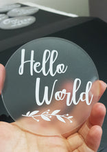 Load image into Gallery viewer, Frosted Clear Acrylic Milestone Disc with White Hello World and White Leaf Detail
